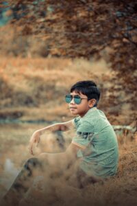 a young man sitting in a field wearing sunglasses